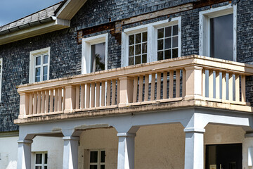 An ancient tenement house with stone tiles on the facade and a terrace upstairs with concrete panels.