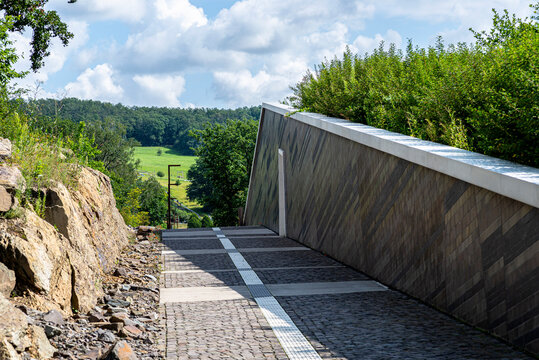 An alley of cobblestones going between the rocks and the wall of the building in the background a field with trees.