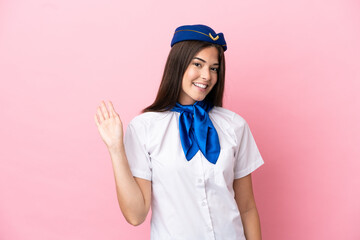Airplane stewardess Brazilian woman isolated on pink background saluting with hand with happy expression