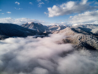 Fototapeta na wymiar Aerial view, sea of fog and clouds illuminated by the rising sun, snow on the tops of the mountains. Russia