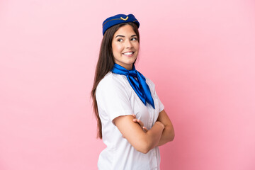 Airplane stewardess Brazilian woman isolated on pink background with arms crossed and happy