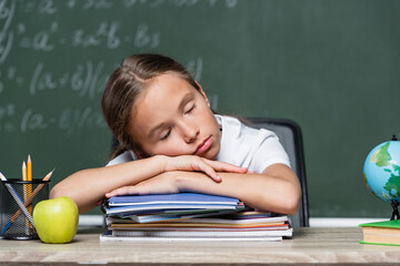 tired schoolgirl sleeping on notebooks near globe and apple on desk
