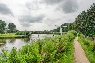 Narrow gravel footpath along and wooden drawbridge across Berkelsche Zweth canal in Lansingerland, the Netherlands