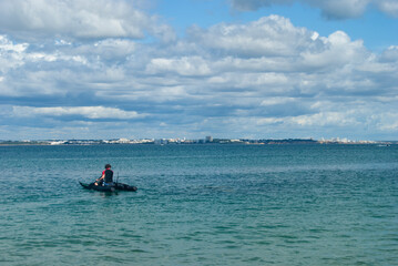 A man sailing at the catamaran in the ocean water, gorgeous cloudy sky and a city in the background