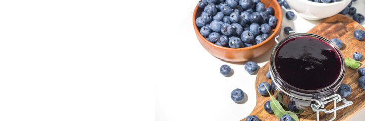 Sweet homemade blueberry jam in small glass jar on a white background, with fresh berries copy space