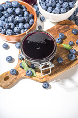 Sweet homemade blueberry jam in small glass jar on a white background, with fresh berries copy space