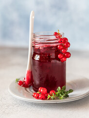 Glass jar with red currant jelly or jam and fresh red currant berries.