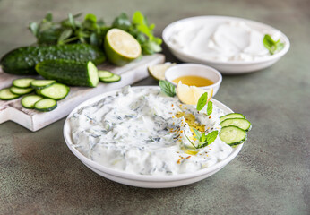 Traditional greek tzatziki dip sauce with grated cucumber, greek yogurt, olive oil and mint, green concrete background.