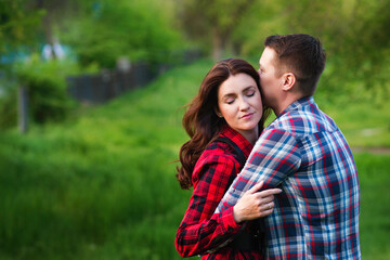 Loving couple hugging while walking relaxing in summer park together. Girlfriend and boyfriend having fun outdoors, kissing and hugging, love concept.
