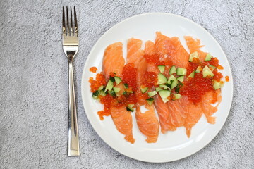 Salmon, red caviar, arugula and fresh cucumber salad on gray background