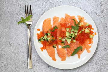 Salmon, red caviar, arugula and fresh cucumber salad on gray background
