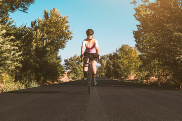 A young female cyclist riding her bike on the asphalt with trees on either side. Cycling concept. Sport concept.