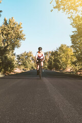 Fototapeta premium A young female cyclist riding her bike on the asphalt with trees on either side. Cycling concept. Sport concept.