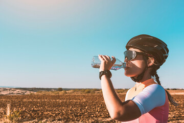 A female cyclist drinks water from a bottle during sunset. Cycling concept. Sport concept.