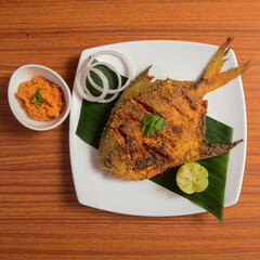 Pomfret fish tawa fry garnished with lemon and onion in a white ceramic plate with wooden...