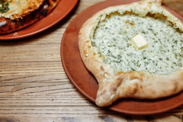 Khachapuri Made From a Delicious Tender Dough with Spinach, Melted Cheese and Butter Close Up. Traditional Hachapuri Topped with Spinacia Leaves on Wooden Rustic Background