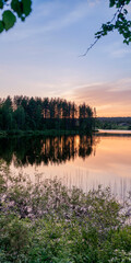 Fototapeta na wymiar Beautiful sunset on a calm lake surrounded by forest in the taiga. Vertical format.