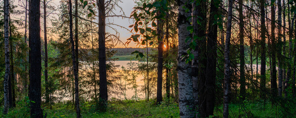 Beautiful sunset on a calm lake surrounded by forest in the taiga. Banner.
