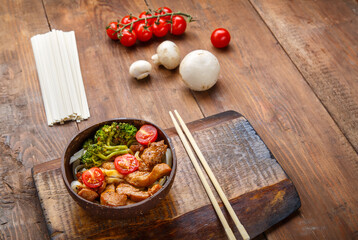 Udon with chicken in Japanese sauce on a plate of coconut shells on a stand next to vegetables.