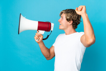 English man over isolated blue background shouting through a megaphone to announce something in lateral position