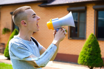Young smiling caucasian guy with amputated arm and prosthesis man shouting into a megaphone while...