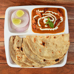 Tandoori roti served with chicken tikka masala, isolated over a rustic wooden background, selective focus