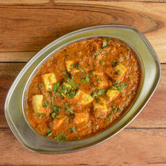 Paneer Butter Masala or Cheese Cottage Curry, served over a rustic wooden background, selective focus