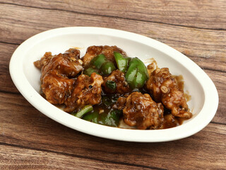 Gobi Manchurian, Popular indo-chinese food made of cauliflower florets, served in a white plate over a rustic wooden table. selective focus