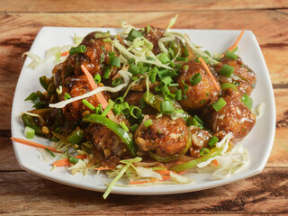 Gobi Manchurian, Popular indo-chinese food made of cauliflower florets, served in a white plate over a rustic wooden table. selective focus
