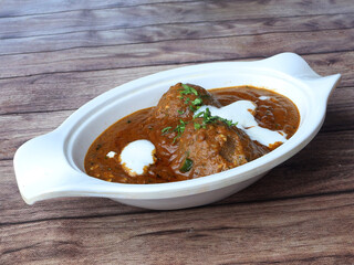 Veg Kofta Curry - classic North Indian vegetarian recipe alternative to meatballs served with tandoori roti or indian bread, served in a white bowl over a rustic wooden table. selective focus
