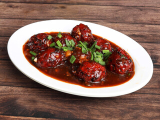 Veg Manchurian, Popular indo-chinese food made of cauliflower florets and other vegetable, served in a white plate over a rustic wooden table. selective focus