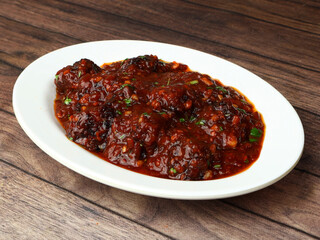 Veg Manchurian, Popular indo-chinese food made of cauliflower florets and other vegetable, served in a white plate over a rustic wooden table. selective focus