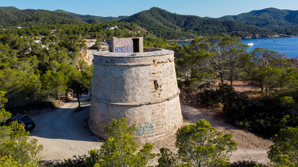 Fototapeta na wymiar Aerial view of the round Tower (Torre) of Portinatx on the north shore of Ibiza island in Spain - Pine forests and rocky cliffs in the Balearic Islands