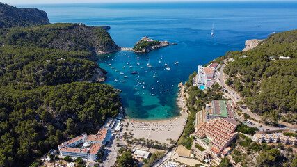 Naklejka premium Aerial view of the beach of Port Sant Miquel on the north shore of Ibiza island in Spain - Isolated bay sided with large hillside hotels in the Balearic Islands