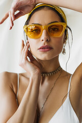 Naklejka premium pretty woman in stylish sunglasses and yellow headscarf posing on white