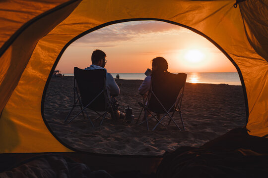 young adults couple looking on sunrise drinking coffee sitting in camping chair