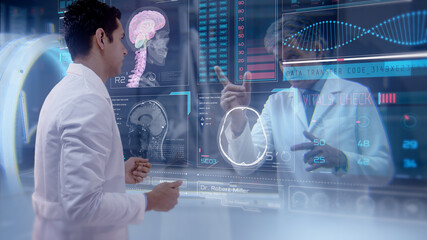 Two doctors having an online video conference analyze a patient's medical MRI diagnosis by checking on a large glass screen with futuristic holograms. Concept of: medicine, doctors, future, holography