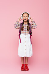 Positive schoolkid holding wireless headphones on pink background