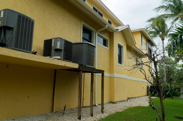 View of a long yellow and white building showing air handler units or air conditioners on exterior of building in florida with palm trees