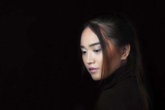 Profile Of Asian Woman Looking Down With Black Turtleneck On Black Background.