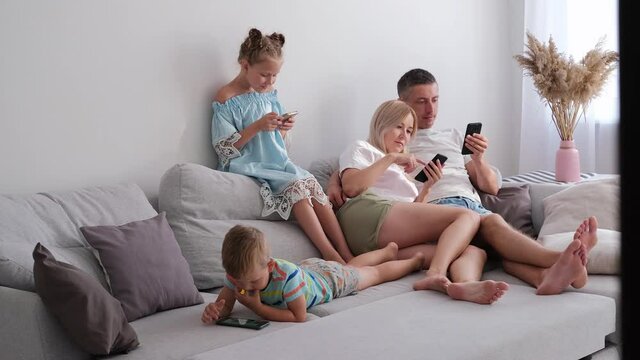 Concentrated members of family sit together on one sofa obsessed with gadgets overuse social media, people internet technology dependence concept. Each of them has phone in hands. They look at them. 