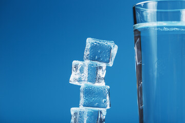 A glass of ice and clear water, ice cubes on a blue background.