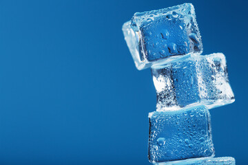Ice cubes with water drops tower in a row on a blue background.