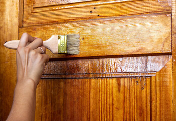 Beautiful young girl paints a wooden door. Summer work in the garden.