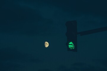 Green traffic light in darkness on night sky and moon in bloor