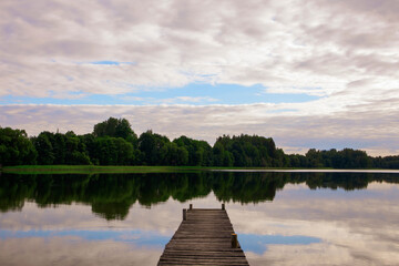 Lake in the evening before sunset with an old wooden footbridge in the center of the picture. Cloudy weather in summer