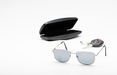 Pair of dark sunglasses with hard protective case and auto key fob on white background