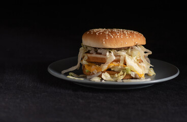 Fast food hamburger plated on a grey saucer on dark background....