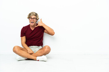 Obraz premium Young English man sitting on the floor making phone gesture. Call me back sign
