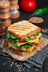 Grilled sandwich with ham, cheese and fresh vegetables on a dark background with ingredients and spices. Vertical view.
